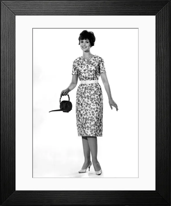 Framed Print : Reveille Fashions: Ann Cave wearing floral summer dress and holding a watering can