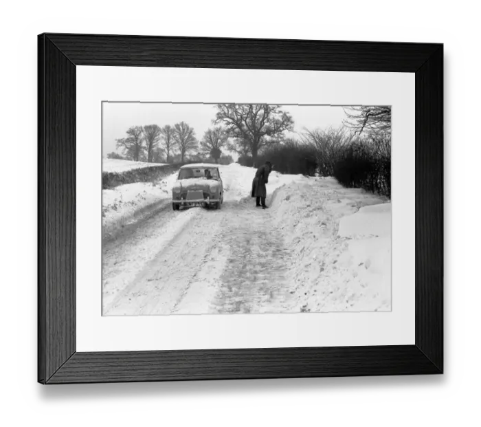 Framed Print : A mini car drives along a snowy lane in the countryside near Coventry whilst a man tries Framed Print : A mini car drives along a snowy lane in the countryside near Coventry whilst a man tries