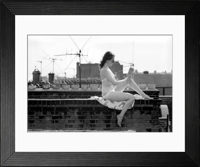 Framed Print : A model wearing a bikini reading a book as she sunbathes on a rooftop on Kings Road in