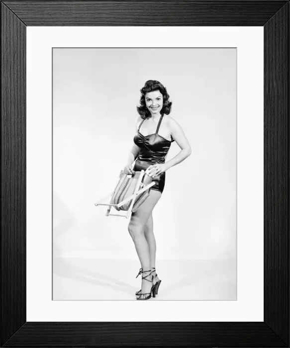Framed Print : Clothing: Fashion: Beachwear. Model wearing swimming costume carrying deck stool Framed Print : Clothing: Fashion: Beachwear. Model wearing swimming costume carrying deck stool