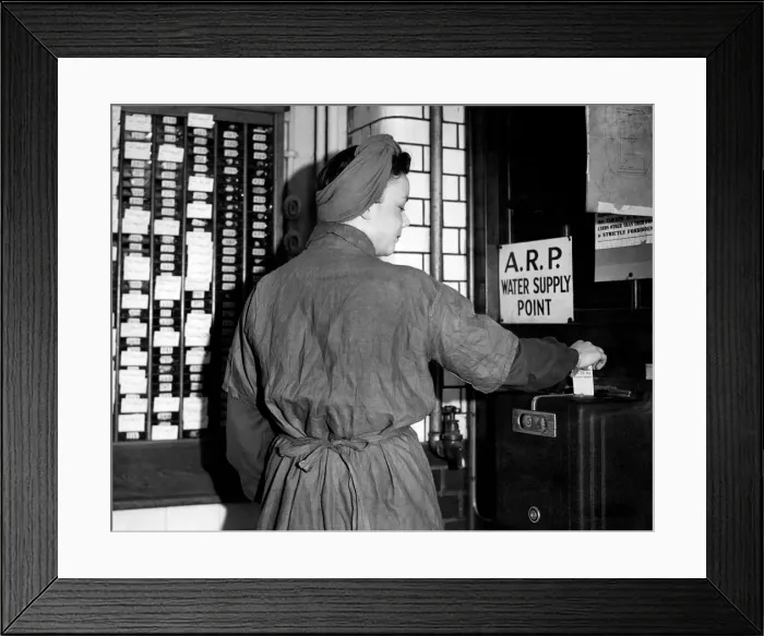 Framed Print : A worker clocking in for her shift at an arms factory in England during the war