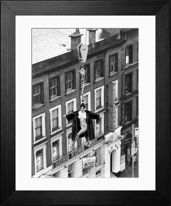 Framed Print : Model Linn Yamazaki demostrating the strength of her hair by hanging above rooftops on a Framed Print : Model Linn Yamazaki demostrating the strength of her hair by hanging above rooftops on a