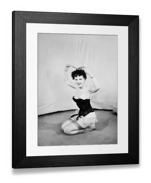 Framed Print : Clothing: Fashion: Underwear: Woman wearing corsett placing bow in hair. 1959