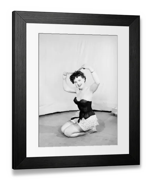 Framed Print : Clothing: Fashion: Underwear: Woman wearing corsett placing bow in hair. 1959