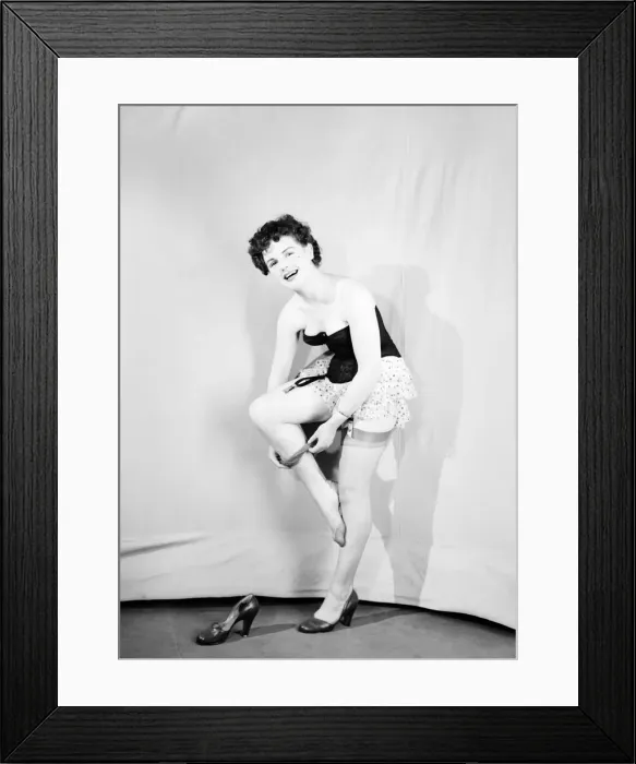 Framed Print : Clothing: Fashion: Underwear: Woman wearing corsett placing bow in hair. 1959