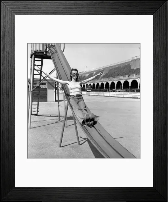 Framed Print : Glamour model wearing a striped vest top and a pair of jeans as she poses on a slide in a Framed Print : Glamour model wearing a striped vest top and a pair of jeans as she poses on a slide in a
