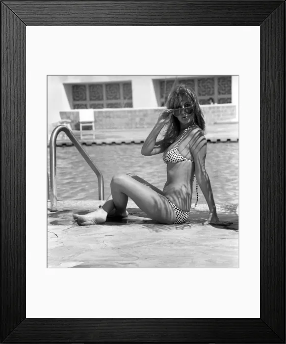 Framed Print : Model wearing a bikini and sunglasses as she sits by the side of a swimming pool in Framed Print : Model wearing a bikini and sunglasses as she sits by the side of a swimming pool in