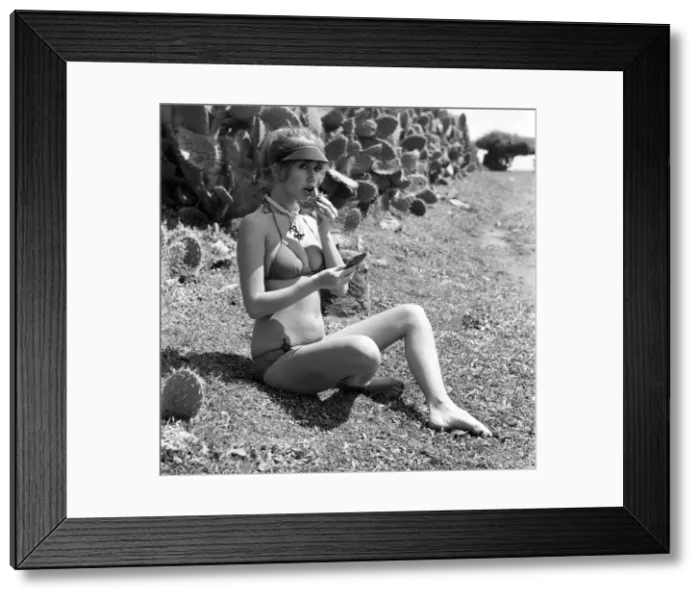 Framed Print : Model putting on her make up as she poses on a beach in Africa wearing a bikini