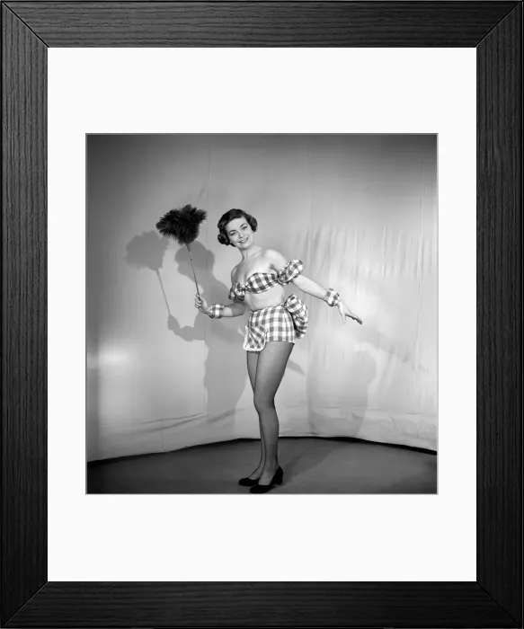 Framed Print : Woman wearing plaid bra and short skirt holding duster. 1959