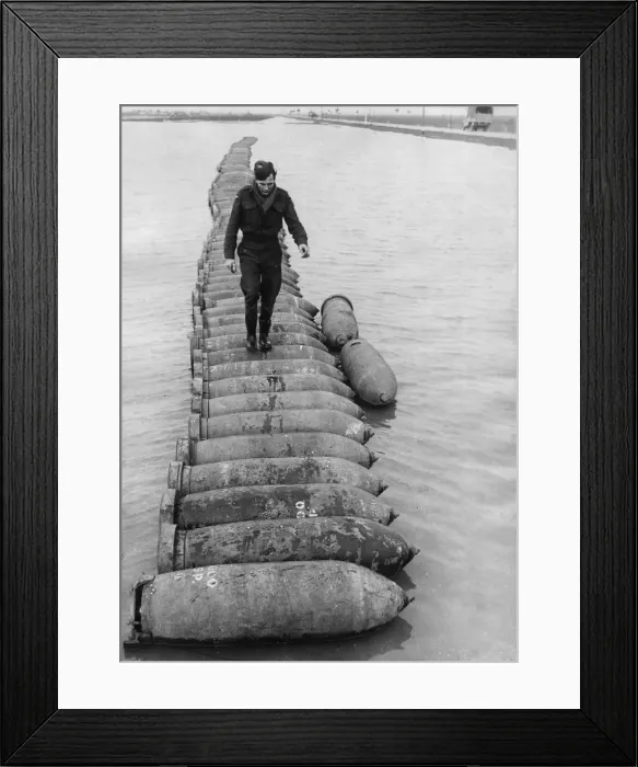 Framed Print : An airman using a line of 1000 lb bombs as a bridge to cross a flooded airfield at an RAF Framed Print : An airman using a line of 1000 lb bombs as a bridge to cross a flooded airfield at an RAF