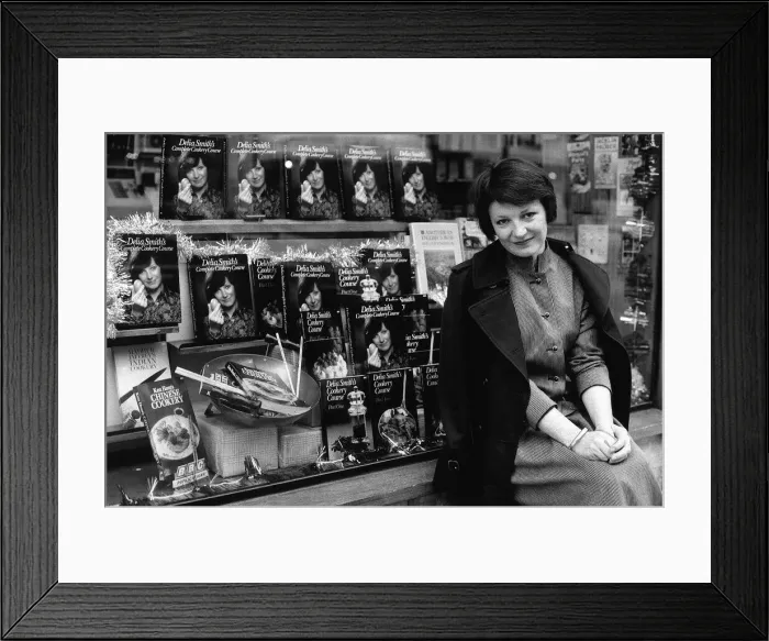 Framed Print : Delia Smith TV Chef and writer sits outside bookshop that has a window full of her books Framed Print : Delia Smith TV Chef and writer sits outside bookshop that has a window full of her books