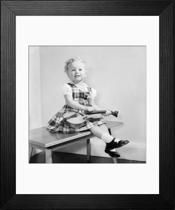 Framed Print : Small girl reading her book also seen with her dolls and violin. 1955 A138 Framed Print : Small girl reading her book also seen with her dolls and violin. 1955 A138