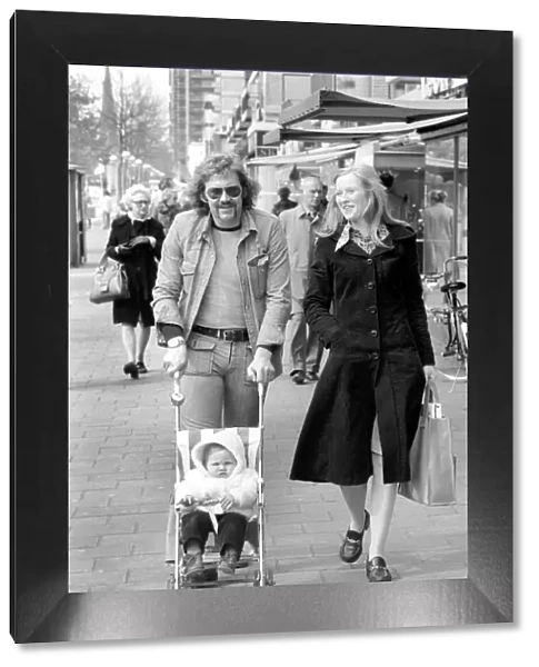 Mother and father pushing their little daughter along in a bugg on the streets of