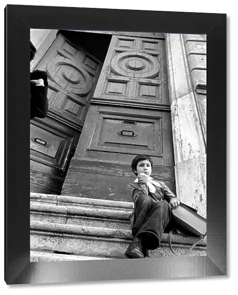 Young child sitting on the steps of an old building in a poor suburb on the outskirts of