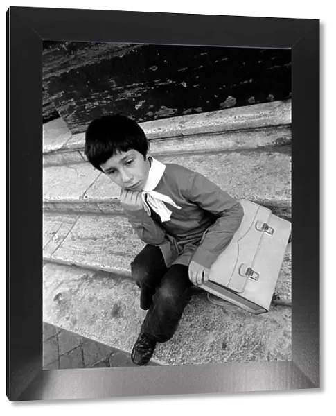 Young child sitting on the steps of his school in a poor suburb on the outskirts of Rome