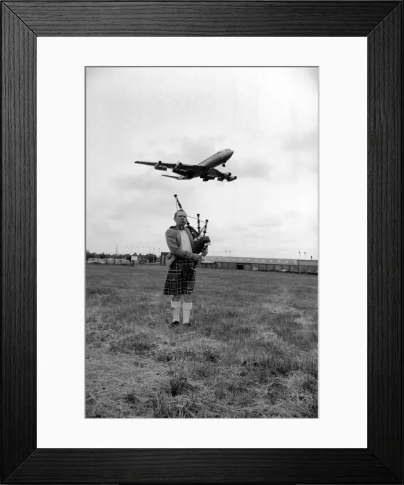 Framed Print : Lone bagpipe player Jim Thomas playing as a jumbo jet flies overhead May 1975