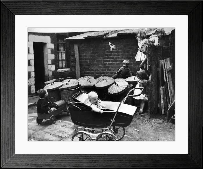 Framed Print : Children play amongst the rubbish bins in the back yard of their houses as a little baby