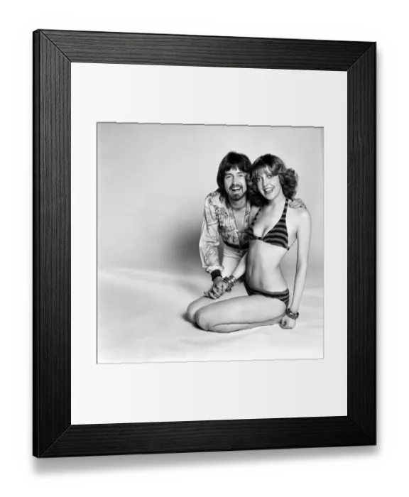 Framed Print : Couple wearing 1970s fashion. The woman wearing a matched striped bikini with the man