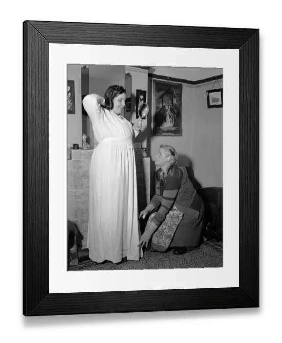 Framed Print : A young woman is giving a helping hand by her mother as she tries on a dress Circa