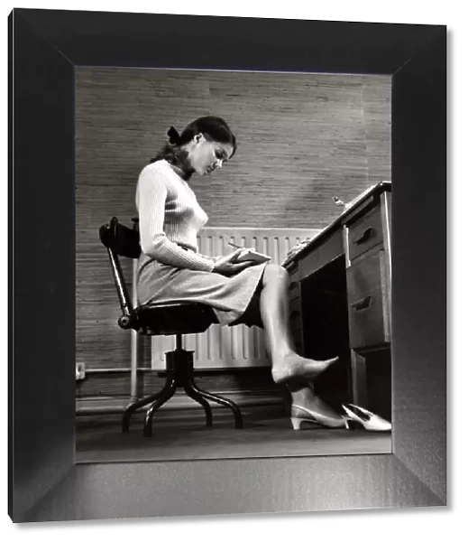 Female office worker sitting taking notes. Writing barefoot  /  taking shoe
