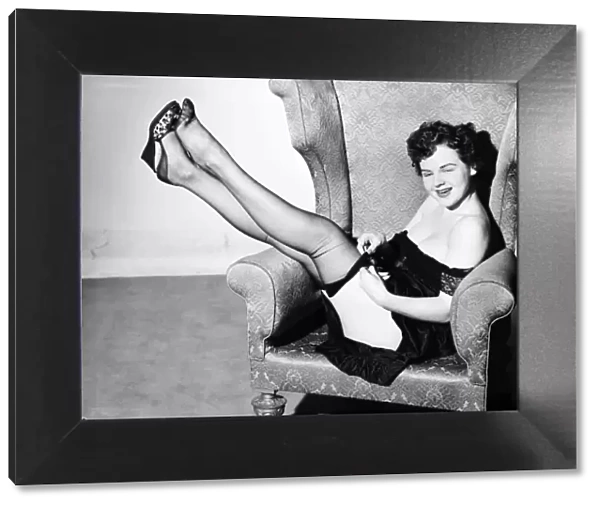 Clothing: Fashion: Stockings and garters. Model sitting in armchair with telephone. E144