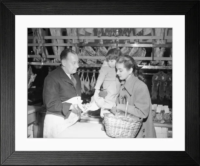 Framed Print : Butcher offers choice cuts of meat to a woman shopper March 1952