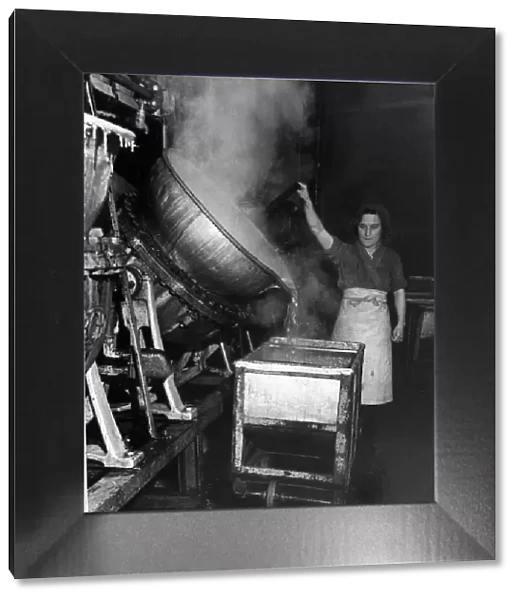 A factory worker tipping a huge cauldron of boiling jam