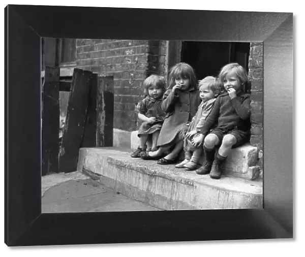 Young children sitting on the doorstep of one of their homes Doris Street, London