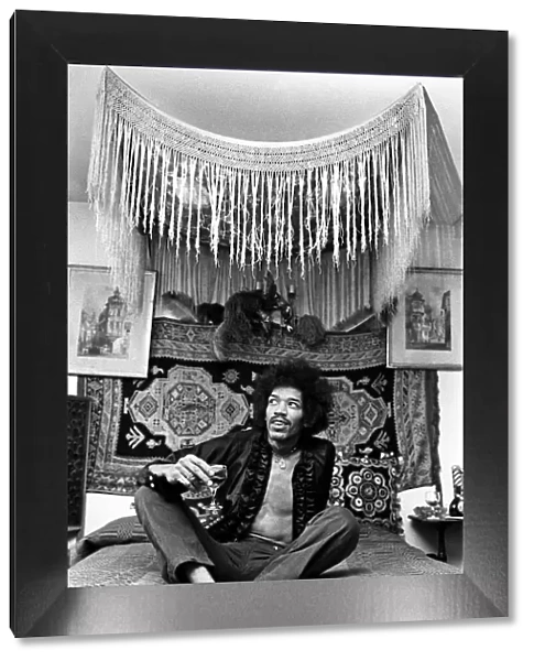 Jimi Hendrix, world famous guitarist, sitting on bed wearing open shirt and necklace