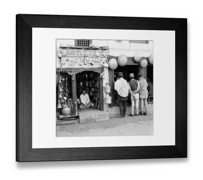 Framed Print : A Nepalese shopkeeper sits in his ironmongers store while shoppers browse his neighbours