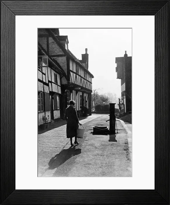 Framed Print : A woman carrying a bucket up the street to get water from a pump. February 1935