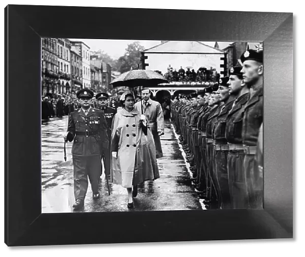 Queen Elizabeth II braves the rain with rain mac and umbrella to inspect a guard of