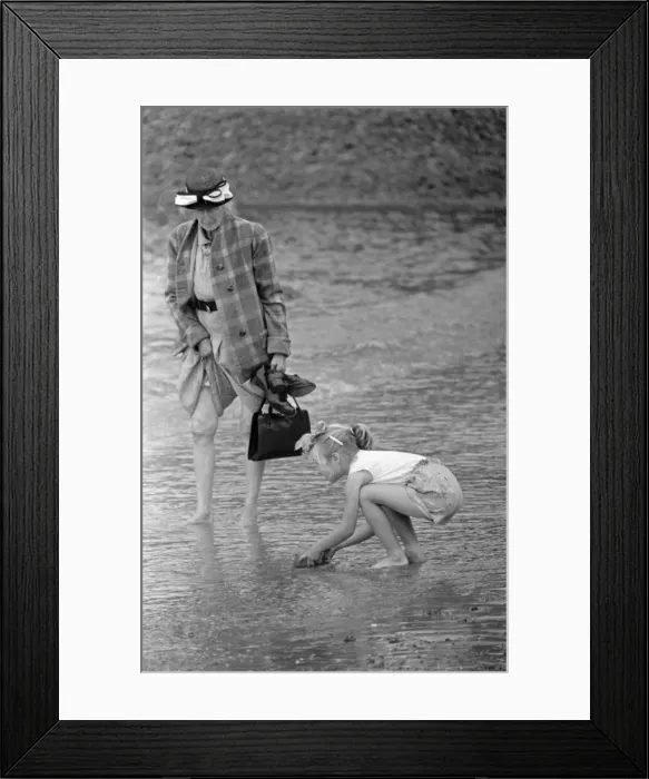 Framed Print : A woman goes for a paddle in the sea as a young gurl picks up a handful of sand