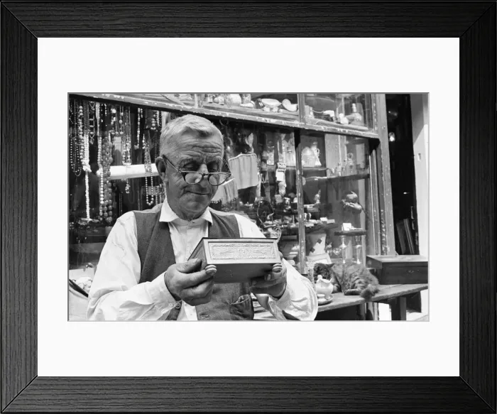 Framed Print : An antique dealers inspects his goods at his shop in The Lanes in Brighton July Framed Print : An antique dealers inspects his goods at his shop in The Lanes in Brighton July