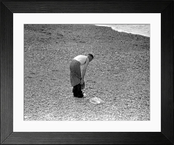 Framed Print : A man getting undressed on the pebble beach at Brighton as he prepares to for a swim Framed Print : A man getting undressed on the pebble beach at Brighton as he prepares to for a swim