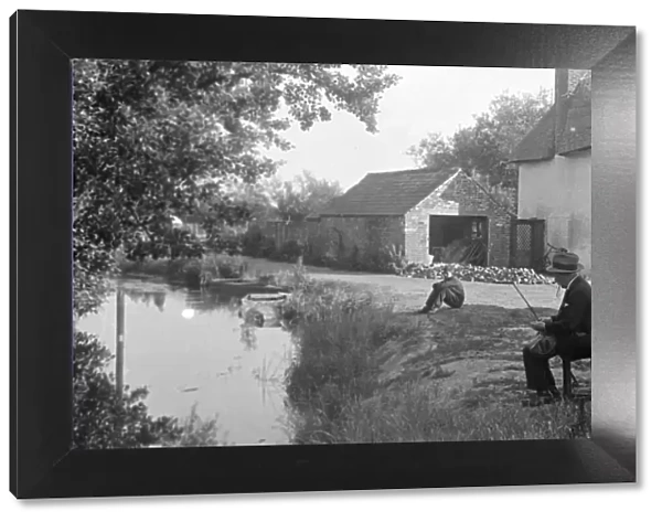 A fisherman prepares his rod beside a river in Kent. Circa 1946