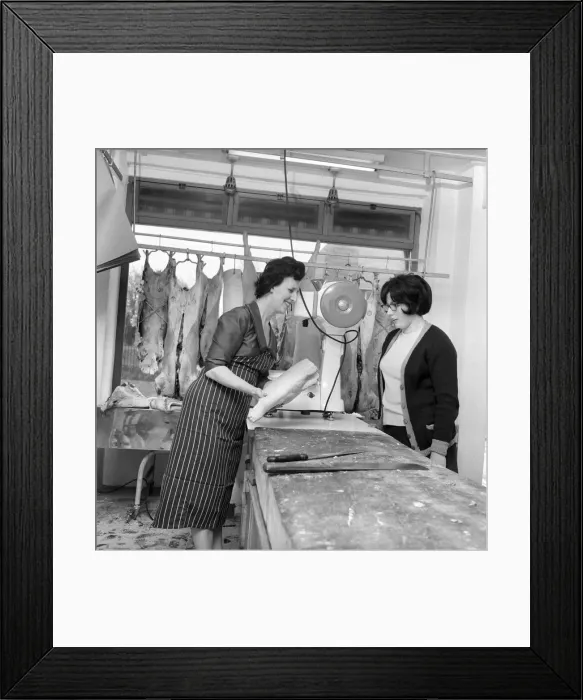 Framed Print : A female butcher seen here at work in her shop, serving a customer at the counter. 1963