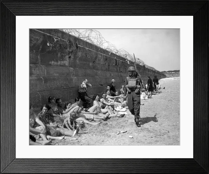 Framed Print : Holidaymakers sunbathing look pityingly at a passing home front serviceman carrying a Framed Print : Holidaymakers sunbathing look pityingly at a passing home front serviceman carrying a