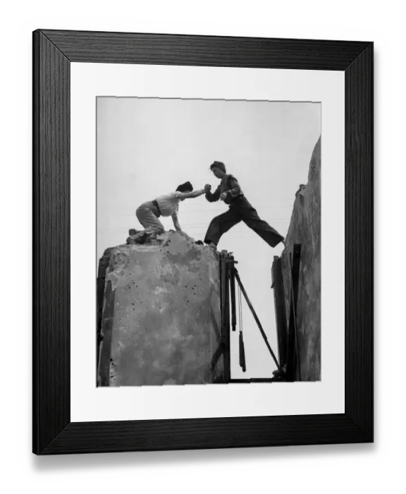 Framed Print : High up on the tottering wall, Lydia Walker steps across the gap aided by Betty Baker