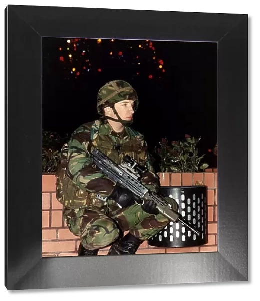 Army Soldier in camouflage uniform standing with a firearm in front of a Christmas tree
