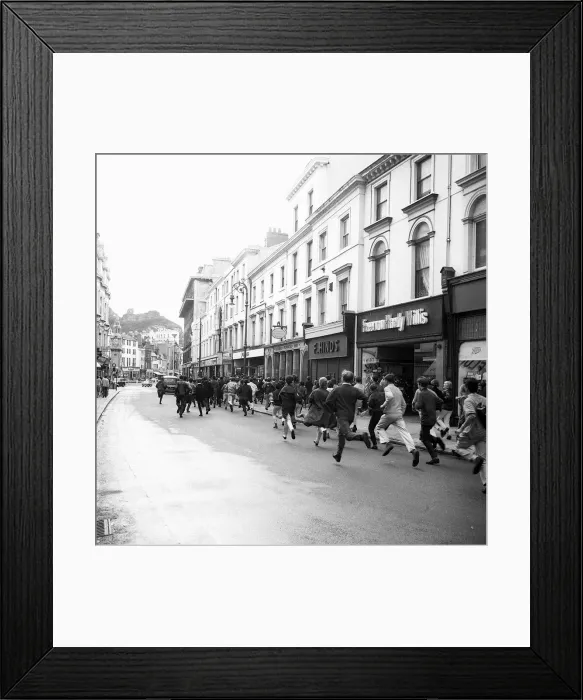 Framed Print : Mods run down the road outside shops in Hastings