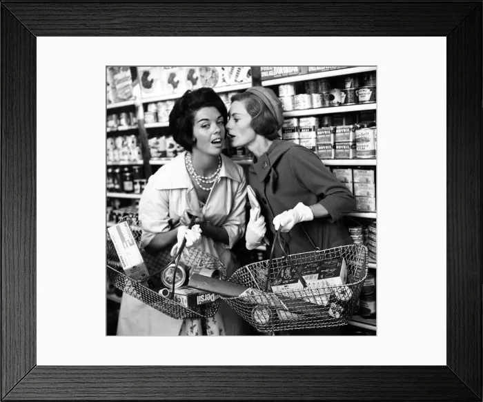 Framed Print : Two women whisper to each other in aisle of shop, 9th September 1960 Framed Print : Two women whisper to each other in aisle of shop, 9th September 1960