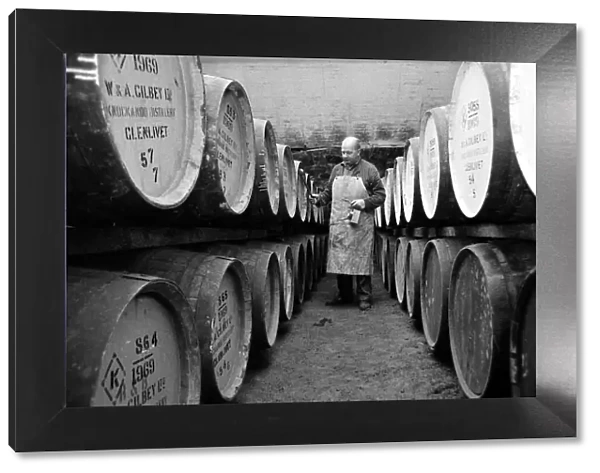 An employee of the Knockando Whisky Distillery in Scotland checks the casks in