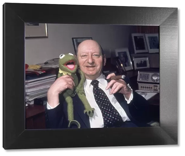 Media Mogul Lew Grade sitting at his desk smoking a cigar while holding Kermit the frog