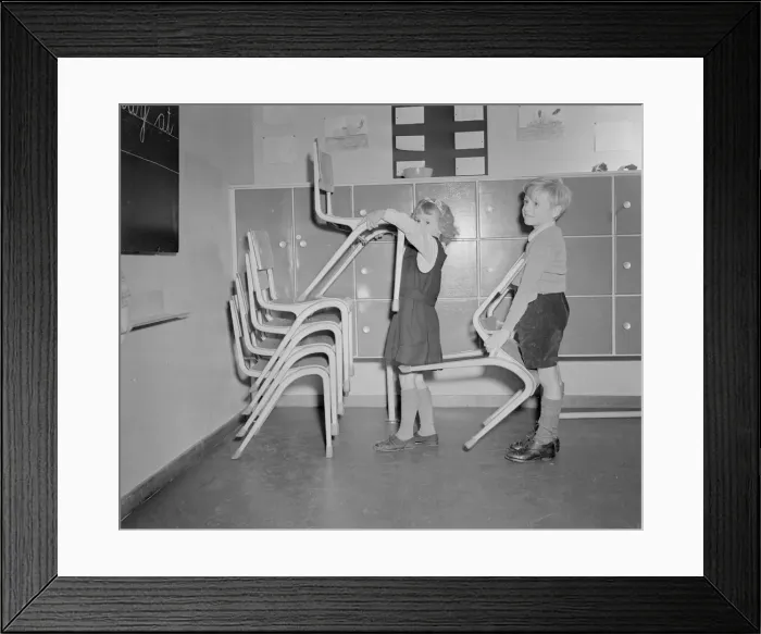 Framed Print : Two pupils seen here stacking chairs following assembly at the new primary school