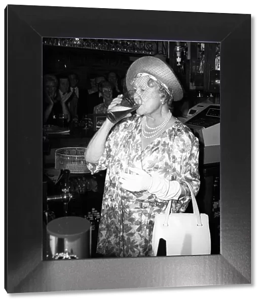 Queen Mother stands behind a pub bar drinking beer in July 1987