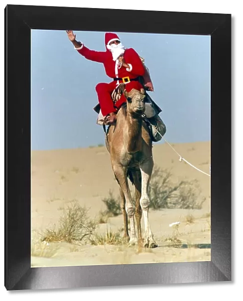 Santa Claus waves from atop his camel in the desert on his way to delivering a message to