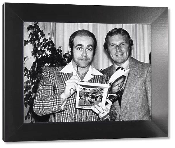 Pop star and chairman of Watford Football Club Elton John helps footballer Bobby Moore