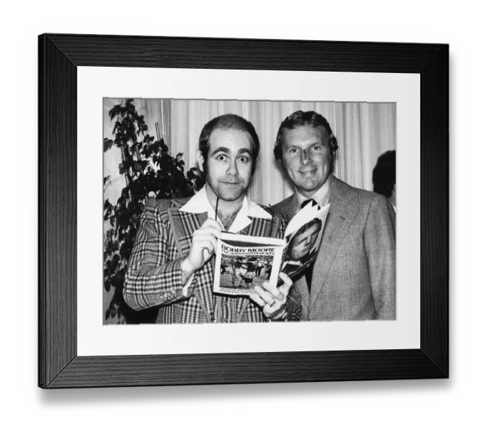 Framed Print : Pop star and chairman of Watford Football Club Elton John helps footballer Bobby Moore