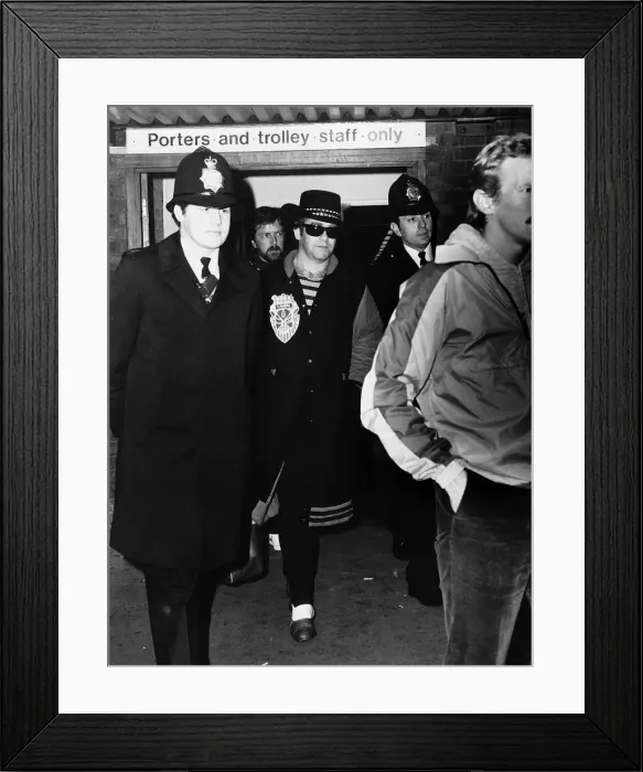 Framed Print : Elton John, pictured at Heathrow Airport, surrounded by police after getting off Framed Print : Elton John, pictured at Heathrow Airport, surrounded by police after getting off
